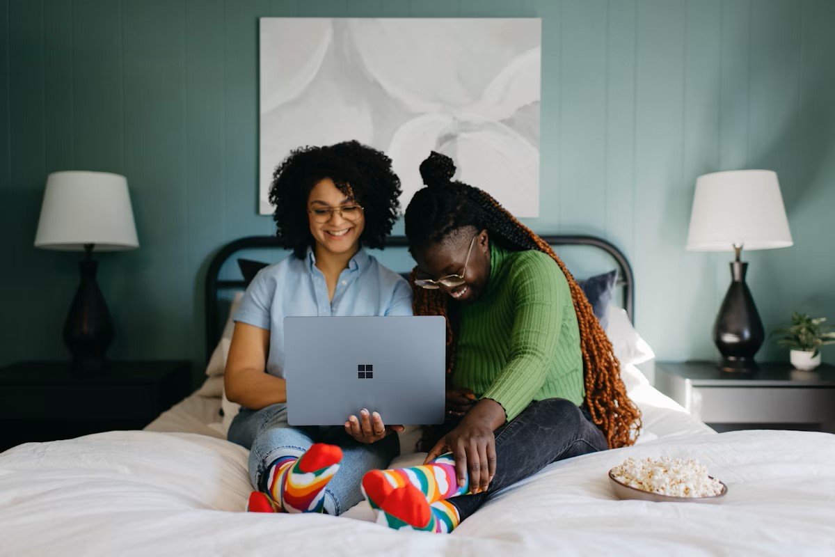 Two women looking at a laptop on a bed, sharing a moment while using the Lunaal app